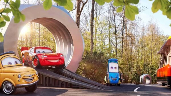 Des voitures animées du film "Cars" entrant dans un grand portail en forme d'aimant sur une route forestière ensoleillée à Disneyland Paris, avec le soleil se couchant en arrière-plan.