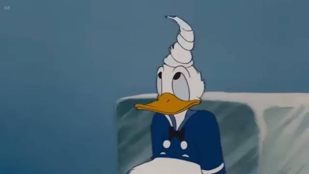 Donald Duck, vêtu d'un costume de marin, a l'air surpris avec un cornet de glace empilé avec humour sur sa tête. Il se tient devant un arrière-plan flou et glacé dans cette scène fantaisiste de Disney.