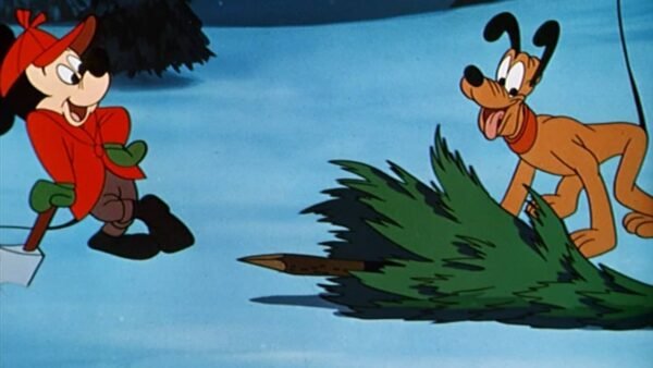 Mickey Mouse, portant un chapeau rouge et des mitaines vertes, se tient à côté d'un sapin de Noël tombé, tandis que Dingo, tenant le sapin, regarde avec une expression enjouée dans un décor enneigé.