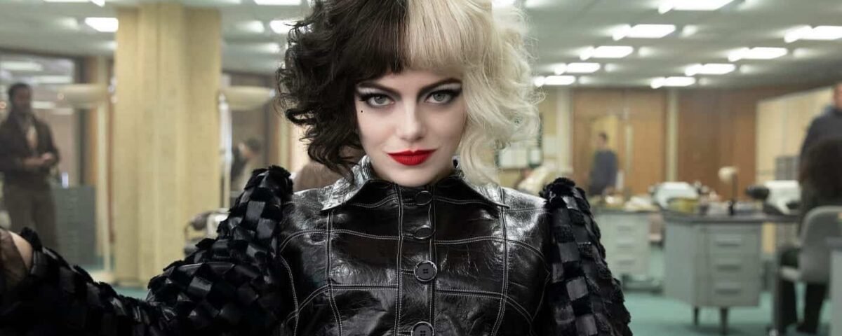 Une femme au maquillage audacieux et aux cheveux bouclés se tient avec confiance dans une robe en cuir et des gants inspirés de Cruella dans un bureau, dégageant une ambiance à la fois ludique et mystérieuse.