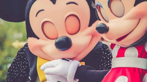 Personnages de Mickey Mouse et Minnie Mouse posant de manière ludique à Disneyland Paris, avec Minnie chuchotant à l'oreille de Mickey, tous deux vêtus de leurs costumes emblématiques.