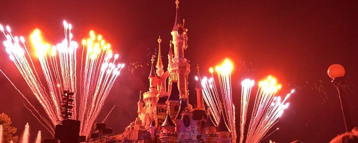 Une scène nocturne à Disneyland Paris avec un feu d'artifice vibrant au-dessus du château, illuminant le ciel d'éclats de lumière blanche et mettant en valeur l'architecture détaillée du château.