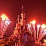 Une scène nocturne à Disneyland Paris avec un feu d'artifice vibrant au-dessus du château, illuminant le ciel d'éclats de lumière blanche et mettant en valeur l'architecture détaillée du château.