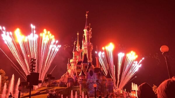 Une scène nocturne à Disneyland Paris avec un feu d'artifice vibrant au-dessus du château, illuminant le ciel d'éclats de lumière blanche et mettant en valeur l'architecture détaillée du château.