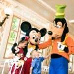 Une interaction joyeuse avec une jeune fille et un garçon rencontrant Mickey Mouse et Dingo à Disneyland Paris, les enfants portant des tenues sur le thème Disney.