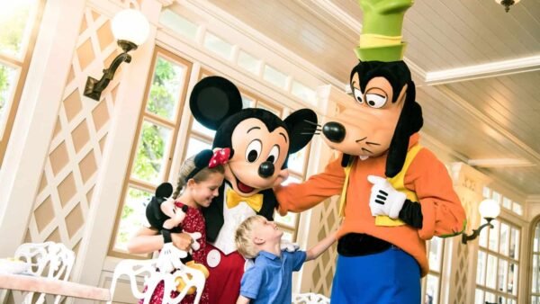 Une interaction joyeuse avec une jeune fille et un garçon rencontrant Mickey Mouse et Dingo à Disneyland Paris, les enfants portant des tenues sur le thème Disney.
