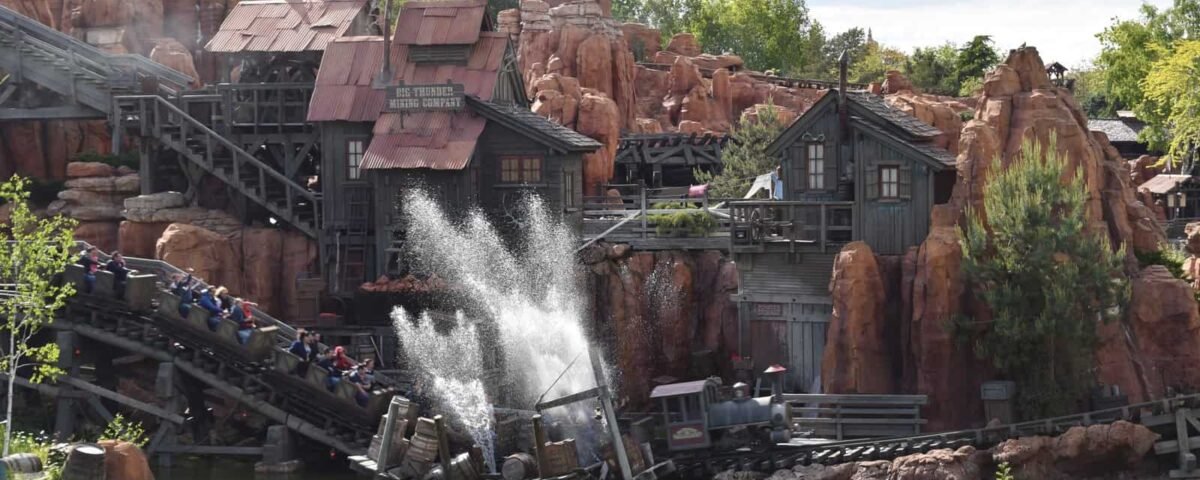 Une balade en rondins à Disneyland Paris avec des passagers descendant dans une pataugeoire, entourée d'un terrain accidenté et rocheux et de bâtiments à thème ressemblant à une ancienne ville minière.