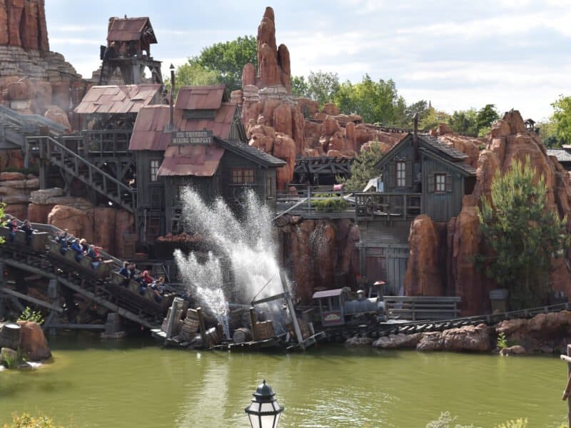 Une balade en rondins à Disneyland Paris avec des passagers descendant dans une pataugeoire, entourée d'un terrain accidenté et rocheux et de bâtiments à thème ressemblant à une ancienne ville minière.