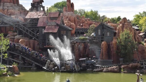 Une balade en rondins à Disneyland Paris avec des passagers descendant dans une pataugeoire, entourée d'un terrain accidenté et rocheux et de bâtiments à thème ressemblant à une ancienne ville minière.