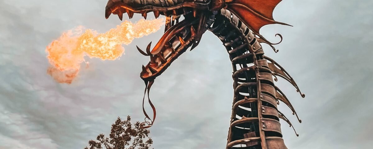 Une grande sculpture de dragon mécanique aux détails complexes, exhalant du feu sur un ciel nuageux, située dans un environnement extérieur entouré d'arbres à Disneyland Paris.