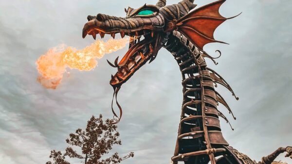 Une grande sculpture de dragon mécanique aux détails complexes, exhalant du feu sur un ciel nuageux, située dans un environnement extérieur entouré d'arbres à Disneyland Paris.