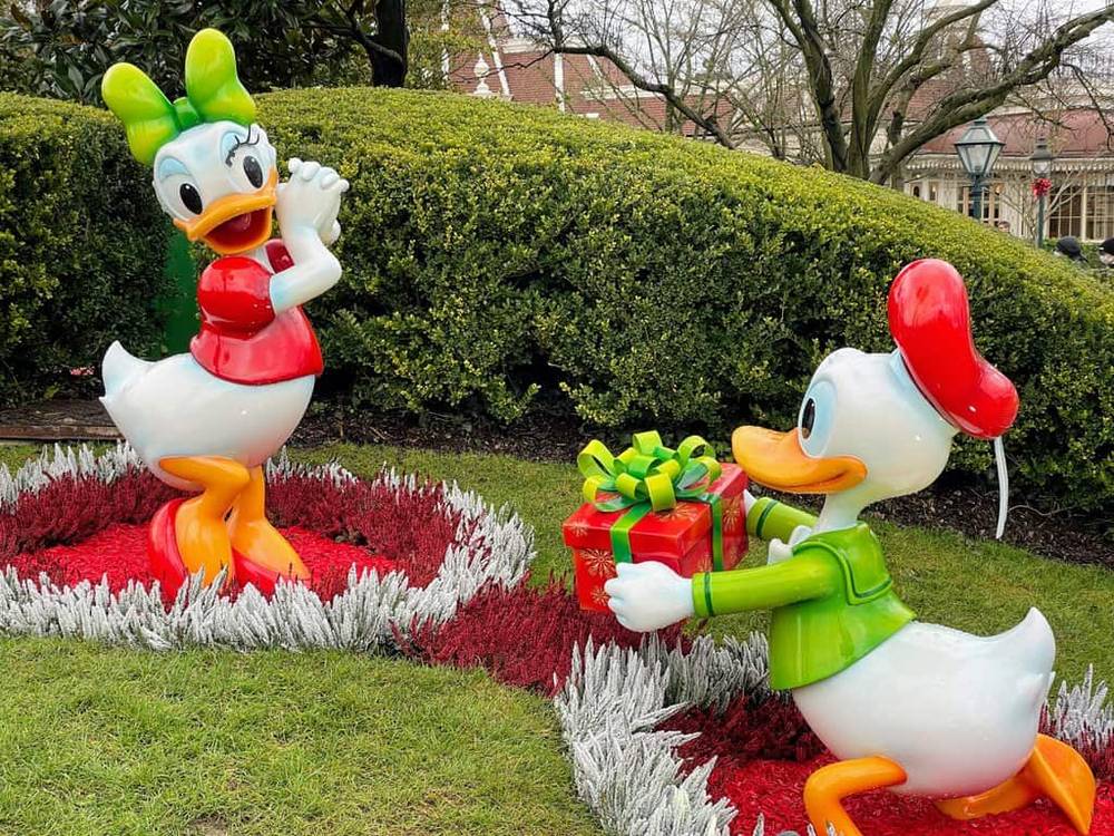 Une paire de figurines de Donald Duck dans un jardin, servant d'adorables souvenirs de Noël aux enfants visitant Disneyland Paris.