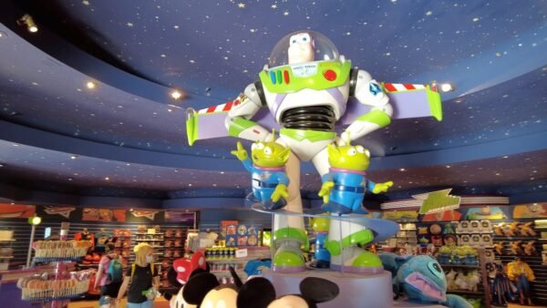 Un grand jouet Buzz l'Éclair entouré de personnages extraterrestres dans un magasin de jouets animé à Disneyland Paris, avec un plafond étoilé présentant des constellations et des étagères de marchandises en arrière-plan.