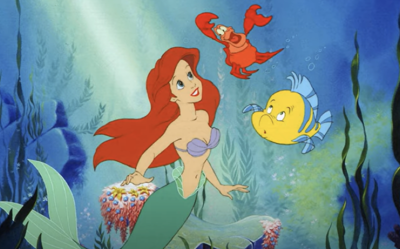 Ariel, la sirène rousse de "La Petite Sirène" de Disney, nage sous l'eau accompagnée de ses amis, le crabe Sébastien et le poisson Flet, sur fond de plantes océaniques et