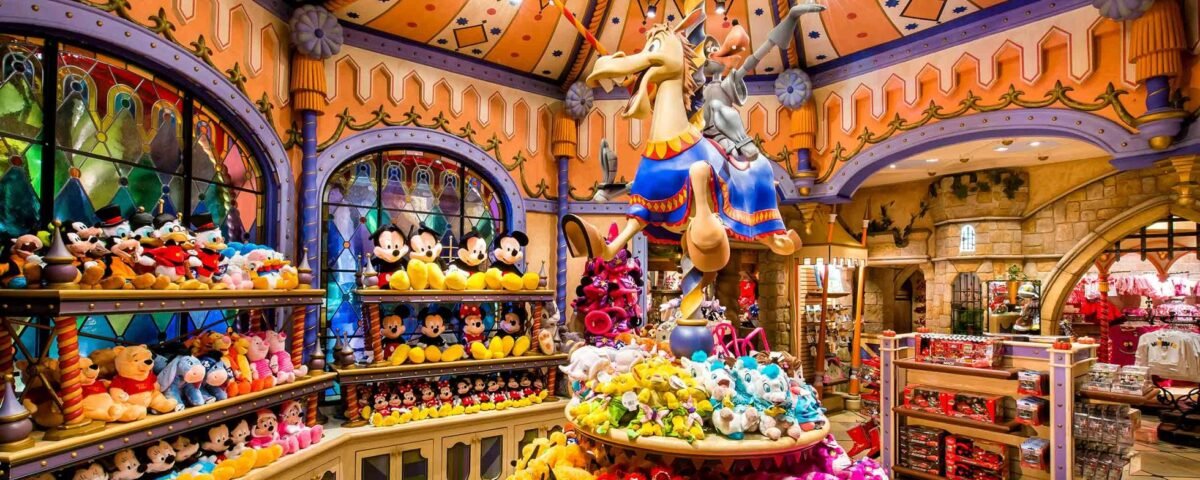 Un magasin de jouets animé avec des étagères colorées remplies de jouets en peluche, comprenant un grand présentoir central de style carrousel avec une figure fantaisiste chevauchant un animal fictif. Une architecture lumineuse et ludique entoure la scène de Sir Mickey