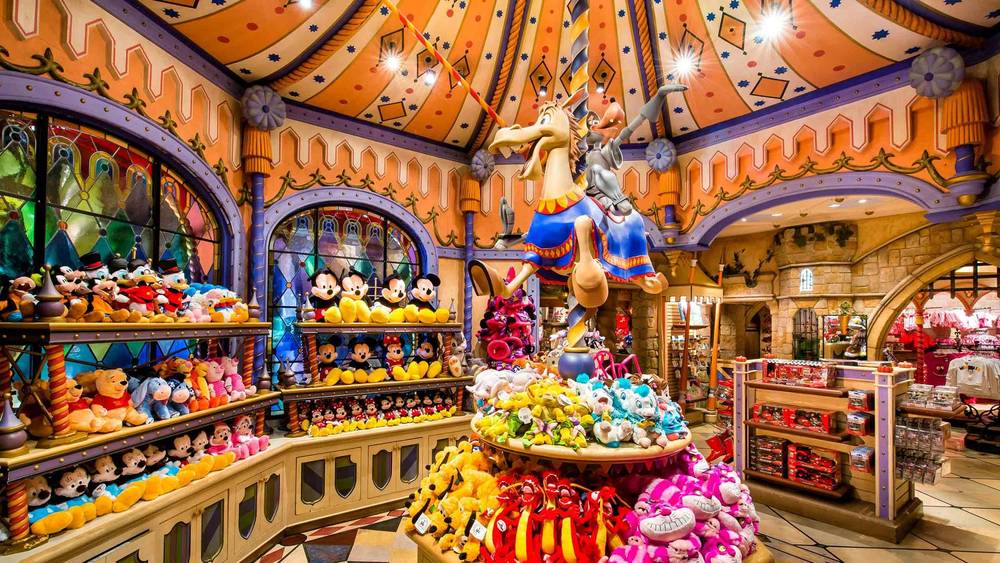 Un magasin de jouets animé avec des étagères colorées remplies de jouets en peluche, comprenant un grand présentoir central de style carrousel avec une figure fantaisiste chevauchant un animal fictif. Une architecture lumineuse et ludique entoure la scène de Sir Mickey