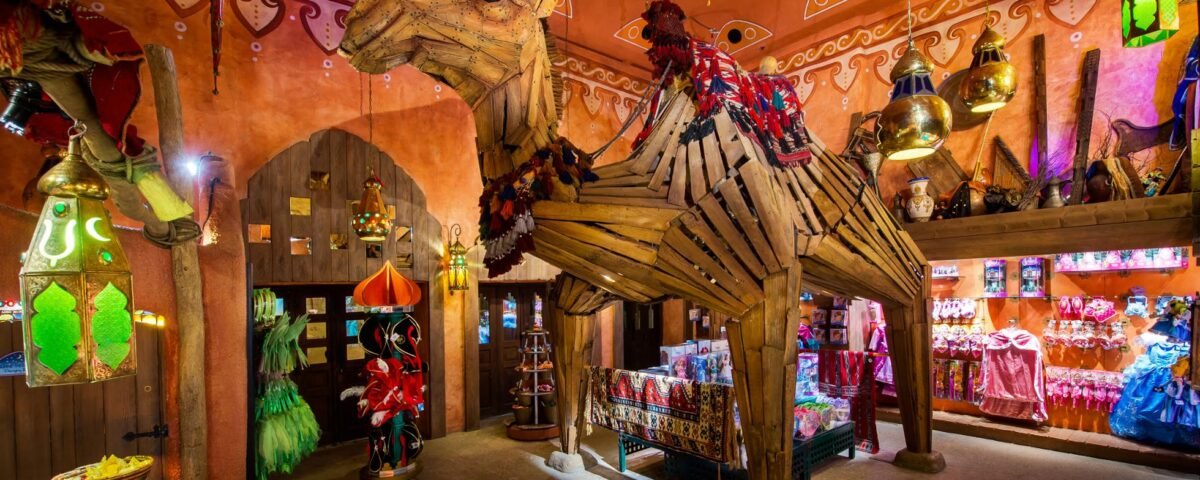 Une boutique vibrante et colorée de Disneyland Paris, Les Trésors de Schéhérazade, présente un modèle de chameau grandeur nature orné de décorations traditionnelles, entouré de lanternes suspendues et d'arcades complexes.