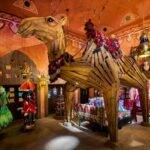 Une boutique vibrante et colorée de Disneyland Paris, Les Trésors de Schéhérazade, présente un modèle de chameau grandeur nature orné de décorations traditionnelles, entouré de lanternes suspendues et d'arcades complexes.
