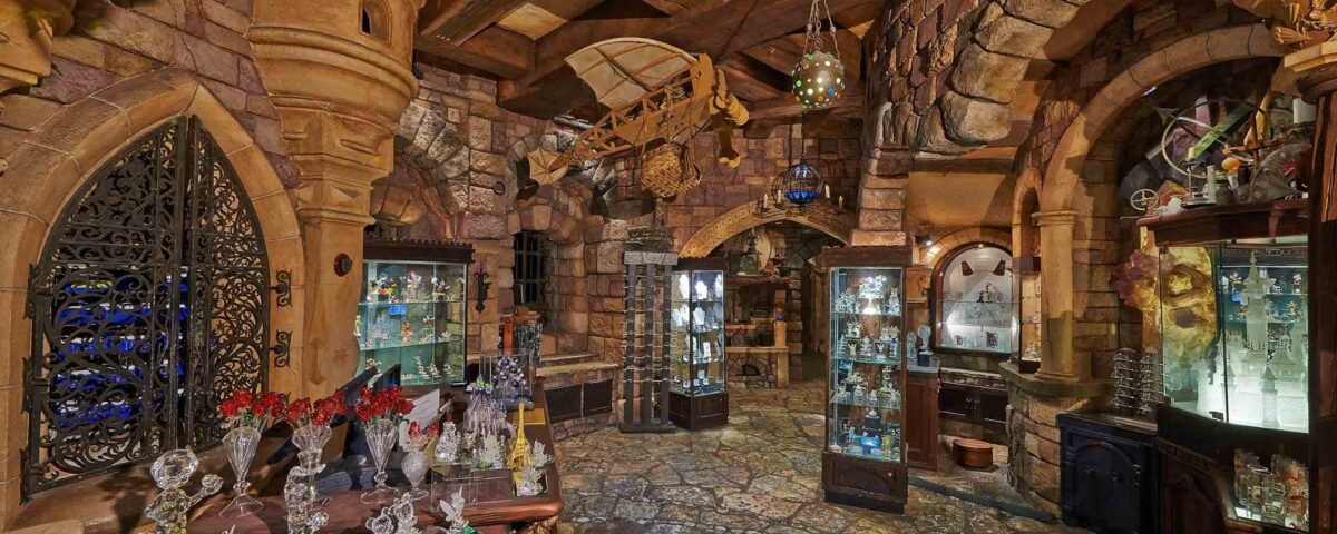Une boutique richement décorée sur le thème médiéval à Disneyland Paris, avec des murs en pierre, des portes cintrées et des marchandises variées exposées dans des vitrines et sur des étagères. Les lanternes suspendues apportent une lueur chaleureuse à la