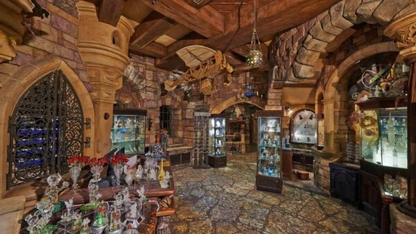 Une boutique richement décorée sur le thème médiéval à Disneyland Paris, avec des murs en pierre, des portes cintrées et des marchandises variées exposées dans des vitrines et sur des étagères. Les lanternes suspendues apportent une lueur chaleureuse à la