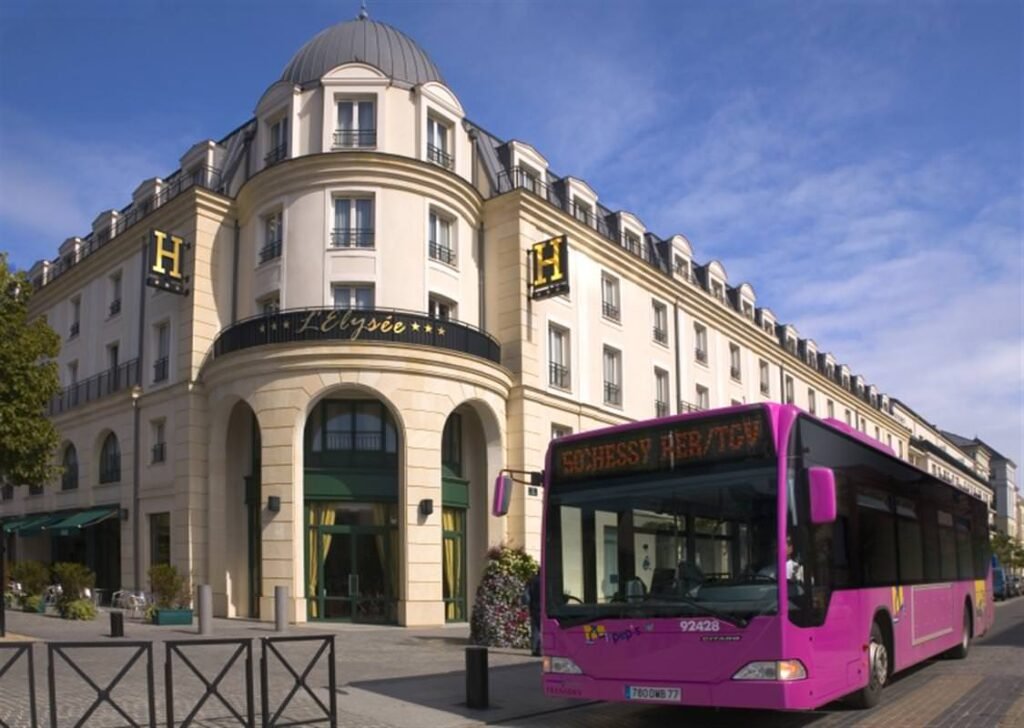 Un bus rose, ressemblant à une des navettes de Disneyland Paris, est garé devant un immeuble.