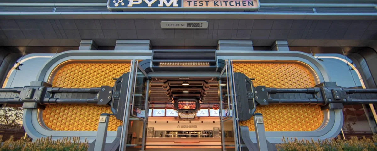 L'entrée de la cuisine PYM à Disneyland Paris, présentant un design élaboré avec des poignées circulaires surdimensionnées qui ressemblent à des boutons de réglage et une façade métallique moderne.