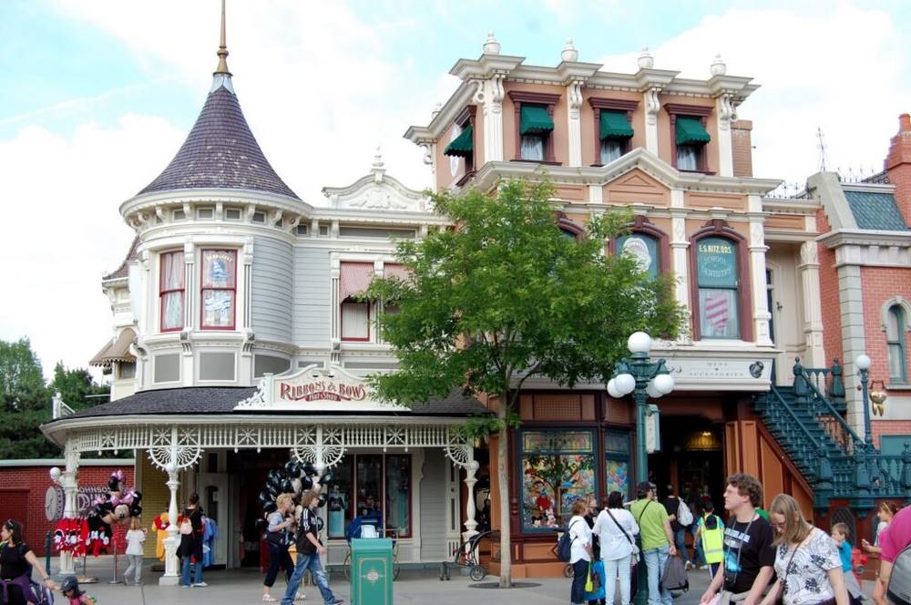 Un groupe de personnes marchant dans une rue de Disneyland, passant devant la boutique de chapeaux Ribbons and Bows à Disneyland Paris.