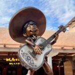 Une statue d'un garçon mexicain jouant de la guitare devant un bâtiment ressemblant à la Casa de Coco à Disneyland Paris.