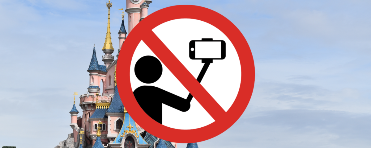 Un panneau d'interdiction sur Disneyland Paris indiquant qu'aucun selfie ou perche à selfie n'est autorisé. Le panneau représente une caméra avec une barre oblique et une personne assise, également barrée.