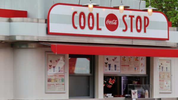 Un kiosque de restauration rapide classique appelé « cool stop » situé dans Disney Village avec un logo Coca-Cola, avec une palette de couleurs rouge et blanche, des panneaux de menu visibles et une glacière à boissons à l'intérieur.