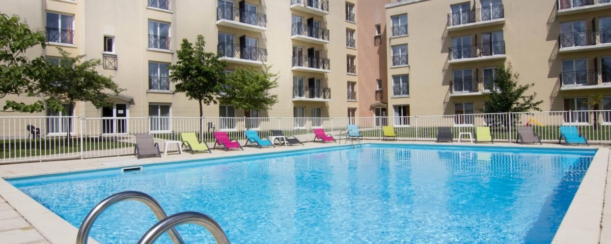 Piscine extérieure de la Résidence du Parc à l'eau bleu clair, entourée de chaises longues et d'une barrière de sécurité, sous un ciel dégagé près de Disneyland Paris.
