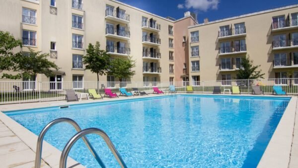 Piscine extérieure de la Résidence du Parc à l'eau bleu clair, entourée de chaises longues et d'une barrière de sécurité, sous un ciel dégagé près de Disneyland Paris.