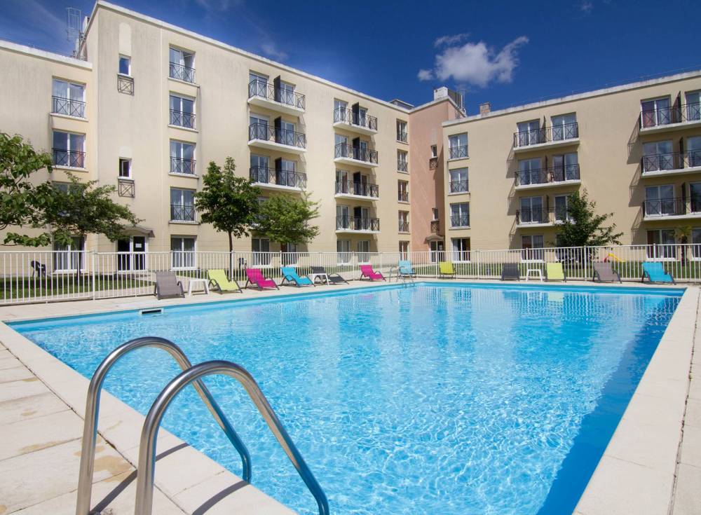 Piscine extérieure de la Résidence du Parc à l'eau bleu clair, entourée de chaises longues et d'une barrière de sécurité, sous un ciel dégagé près de Disneyland Paris.