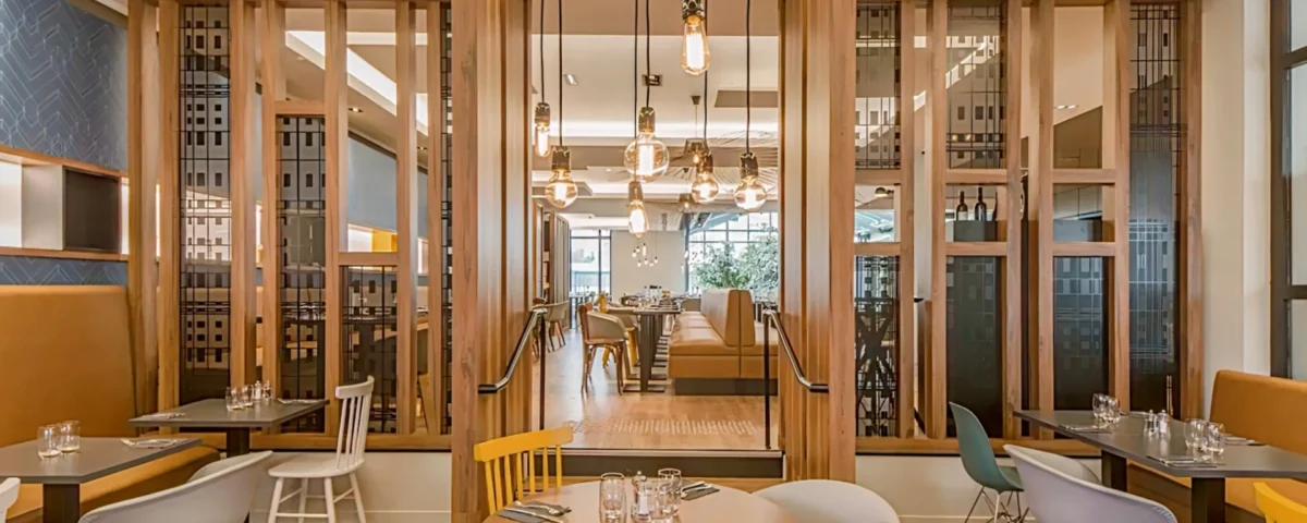 Un intérieur de restaurant moderne et élégant avec d'élégantes cloisons en bois, une variété de sièges avec des chaises colorées, des suspensions suspendues et une atmosphère chaleureusement éclairée près de l'Elysée Val d'Europe.