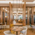 Un intérieur de restaurant moderne et élégant avec d'élégantes cloisons en bois, une variété de sièges avec des chaises colorées, des suspensions suspendues et une atmosphère chaleureusement éclairée près de l'Elysée Val d'Europe.