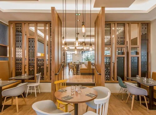 Un intérieur de restaurant moderne et élégant avec d'élégantes cloisons en bois, une variété de sièges avec des chaises colorées, des suspensions suspendues et une atmosphère chaleureusement éclairée près de l'Elysée Val d'Europe.