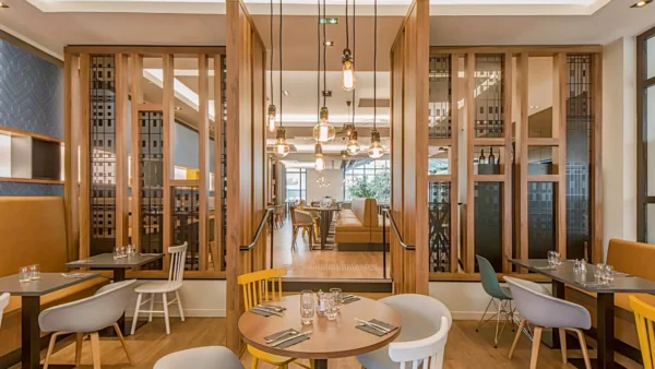 Un intérieur de restaurant moderne et élégant avec d'élégantes cloisons en bois, une variété de sièges avec des chaises colorées, des suspensions suspendues et une atmosphère chaleureusement éclairée près de l'Elysée Val d'Europe.