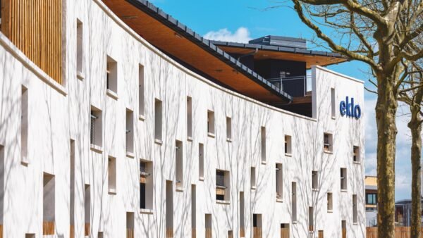 Bâtiment blanc moderne avec des motifs de façade abstraits et le logo « eklo », accompagné d'un arbre nu et d'un ciel bleu.