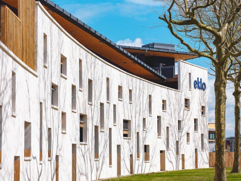 Bâtiment blanc moderne avec des motifs de façade abstraits et le logo « eklo », accompagné d'un arbre nu et d'un ciel bleu.