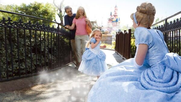 Une jeune fille en costume de princesse court avec enthousiasme vers une femme habillée en Cendrillon en robe bleue à l'Auberge de Cendrillon, avec sa famille souriant derrière elle sous le soleil