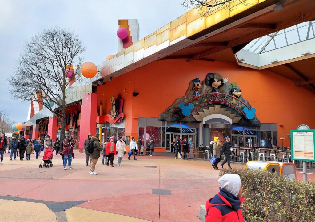 Un groupe de personnes marchant devant un Disney Village, avec l'emblématique Disney Store en arrière-plan.