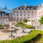 Cour d'un hôtel de luxe avec une élégante pergola en métal, des sièges extérieurs, une fontaine centrale et des haies bien entretenues, dans le contexte de Disneyland Paris.