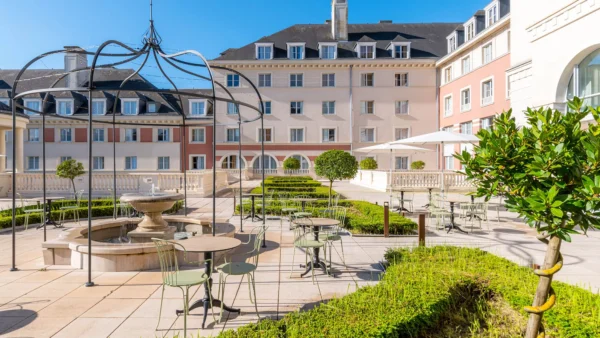 Cour d'un hôtel de luxe avec une élégante pergola en métal, des sièges extérieurs, une fontaine centrale et des haies bien entretenues, dans le contexte de Disneyland Paris.