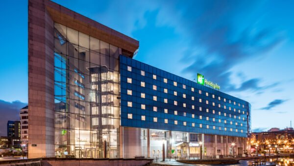 Bâtiment hôtelier moderne éclairé au crépuscule avec une façade en verre, arborant le logo Disneyland Paris, situé au bord d'un plan d'eau calme avec un ciel flou indiquant une longue exposition.
