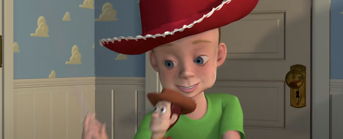 Un jeune garçon au sourire éclatant, coiffé d'un grand chapeau de cowboy rouge et d'un t-shirt vert, tenant joyeusement un jouet Woody du film Toy Story de Pixar dans une pièce au papier peint à motifs de nuages.