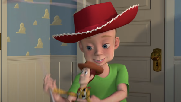Un jeune garçon au sourire éclatant, coiffé d'un grand chapeau de cowboy rouge et d'un t-shirt vert, tenant joyeusement un jouet Woody du film Toy Story de Pixar dans une pièce au papier peint à motifs de nuages.