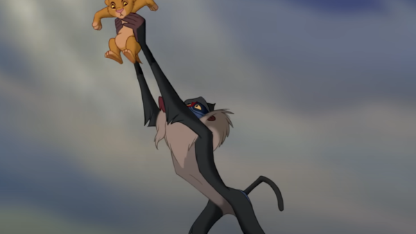 Une scène de "Le Roi Lion" montrant Rafiki tenant Simba en l'air sur Pride Rock sous un ciel dramatique.