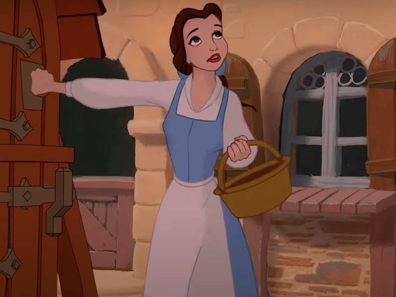 Personnage animé Belle de "La Belle et la Bête" en robe bleue tenant un panier, debout près d'une porte en bois, avec une expression surprise.