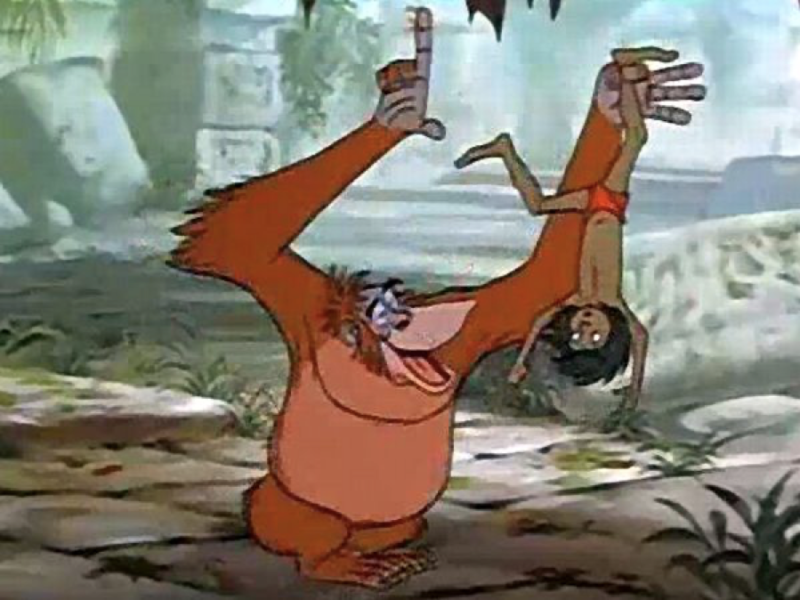 Un orang-outan animé joyeusement suspendu la tête en bas à une vigne de la jungle, agitant une main et tenant un fruit dans l'autre, rappelant une scène du "Livre de la Jungle" de Disney.