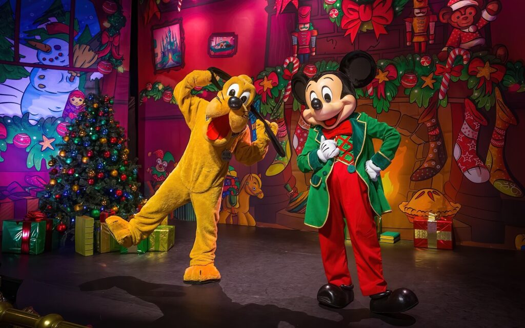 Deux mascottes de Disneyland Paris habillées en Mickey Mouse debout devant un sapin de Noël.